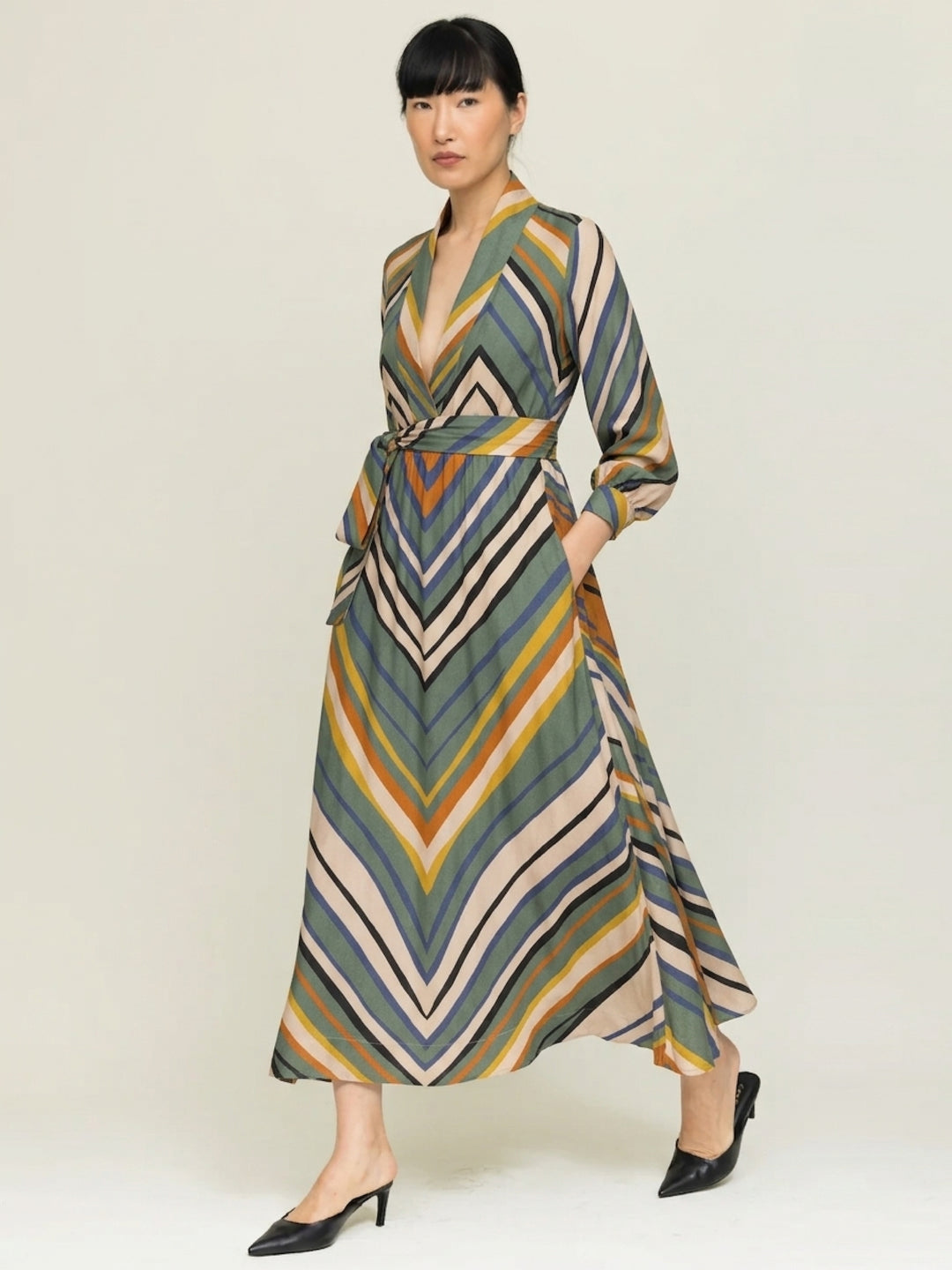 model wearing stripe print wrap dress with  hands in pockets against a neutral background 