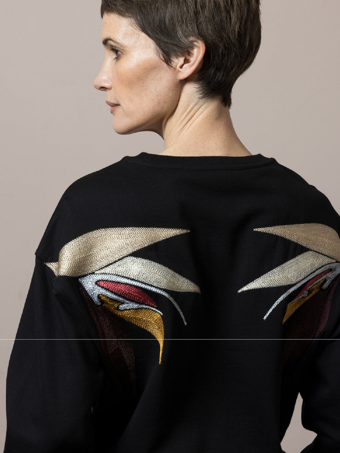 model back view wears  Black sweatshirt cotton fleece with linear embroidery across front and artisan chainstitch embroidery on back 